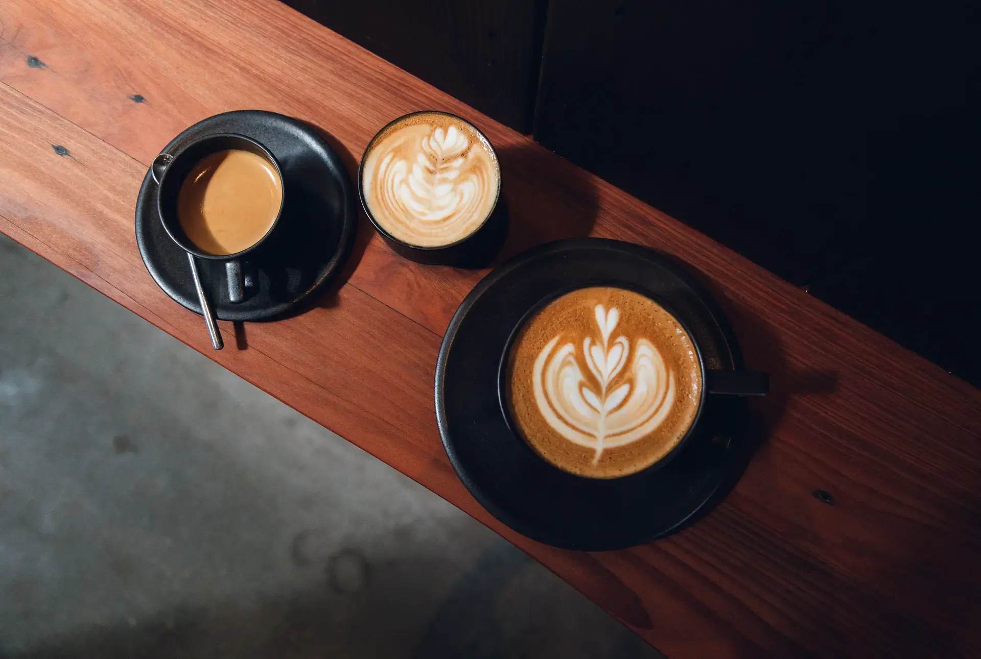 Three craft coffees with latte art on dark wood bar at Ki'bok